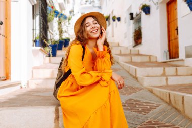 Dağlarda küçük bir kasabada gezen şapkalı ve parlak elbiseli bir kadın turist. Yürüyüşten, havadan ve mimariden hoşlanan güzel bir kadın. Seyahat, yürüyüş konsepti.