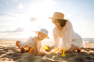 Genç anne ve kızı kumsalda kum inşa ederek eğleniyorlar. Güzel bir kadın ve bir çocuk dışarıda birlikte vakit geçiriyorlar. Çocukluk kavramı, annelik, eğlence..