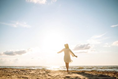 Şapkalı ve güneş gözlüklü güzel bir kadın kumlu sahilde yürüyor ve saçlarıyla rüzgârı yakalıyor. Genç bir kadın güneşli havanın tadını çıkarıyor, deniz manzaralı özgürlüğün tadını çıkarıyor. Keyif ve özgürlük kavramı.