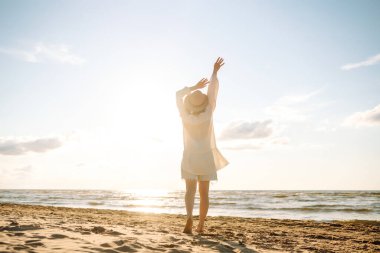 Şapkalı ve güneş gözlüklü güzel bir kadın kumlu sahilde yürüyor ve saçlarıyla rüzgârı yakalıyor. Genç bir kadın güneşli havanın tadını çıkarıyor, deniz manzaralı özgürlüğün tadını çıkarıyor. Keyif ve özgürlük kavramı.