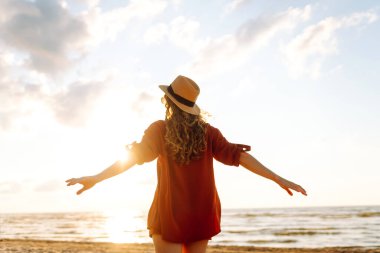 Kıvırcık saçlı genç bir kadının kıyı şeridinde rahat hisseder. Genç bir kadın gün batımında sahilde yürür. Rahatlama, keyif, özgürlük kavramı.