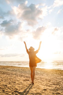 Kıvırcık saçlı genç bir kadının kıyı şeridinde rahat hisseder. Genç bir kadın gün batımında sahilde yürür. Rahatlama, keyif, özgürlük kavramı.