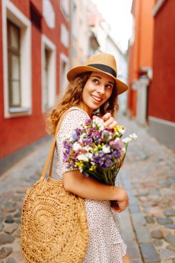 Güneşli Avrupa caddesinde yürüyen şapkalı ve buketi olan güzel bir kadın. Genç turist dışarıda eğleniyor ve eğleniyor. Yürüyen konsept, seyahat.