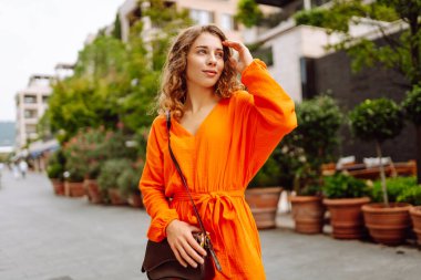 Parlak elbiseli bir gezgin güneşli bir cadde boyunca yürüyor. Etrafta palmiye ağaçları var. Güzel bir kadın havanın ve tatilin tadını çıkarıyor. Turizm, keyif konsepti. Etkin yaşam biçimi.