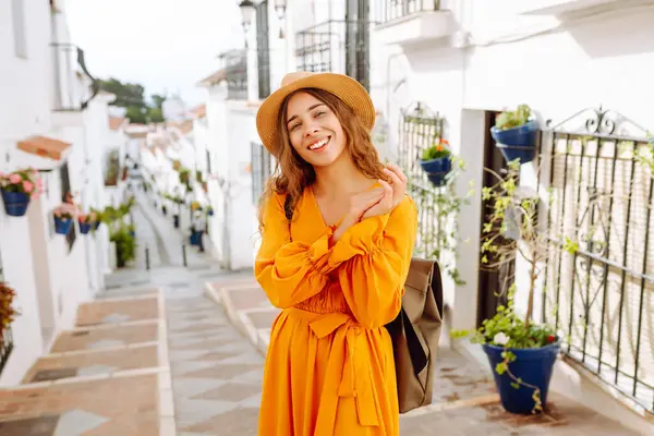 Dağlarda küçük bir kasabada gezen şapkalı ve parlak elbiseli bir kadın turist. Yürüyüşten, havadan ve mimariden hoşlanan güzel bir kadın. Seyahat, yürüyüş konsepti.