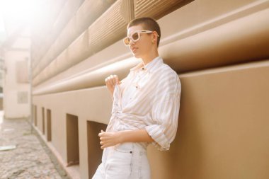 Kısa saçlı şık bir kadın şehrin güneşli sokaklarında poz veriyor. Genç bir turist dışarıda havanın tadını çıkarıyor. Turizm ve moda konsepti.