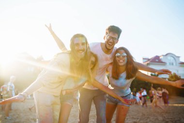 Bir grup neşeli arkadaş renkli bir festivali kutluyor, birbirlerine boya atıyorlar. Genç erkekler ve kadınlar gün batımındaki kumsalın eğlenceli atmosferinin tadını çıkarıyorlar. Kutlama ve eğlence anlayışı.