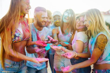 Bir grup neşeli arkadaş renkli bir festivali kutluyor, birbirlerine boya atıyorlar. Genç erkekler ve kadınlar gün batımındaki kumsalın eğlenceli atmosferinin tadını çıkarıyorlar. Kutlama ve eğlence anlayışı.