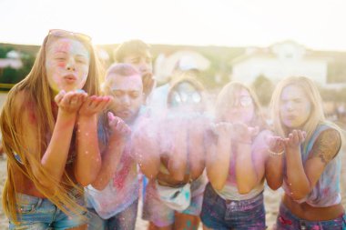 Bir grup neşeli arkadaş renkli bir festivali kutluyor, birbirlerine boya atıyorlar. Genç erkekler ve kadınlar gün batımındaki kumsalın eğlenceli atmosferinin tadını çıkarıyorlar. Kutlama ve eğlence anlayışı.