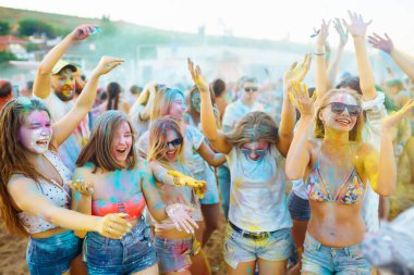 Bir grup neşeli arkadaş renkli bir festivali kutluyor, birbirlerine boya atıyorlar. Genç erkekler ve kadınlar gün batımındaki kumsalın eğlenceli atmosferinin tadını çıkarıyorlar. Kutlama ve eğlence anlayışı.
