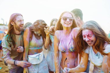 Bir grup neşeli arkadaş renkli bir festivali kutluyor, birbirlerine boya atıyorlar. Genç erkekler ve kadınlar gün batımındaki kumsalın eğlenceli atmosferinin tadını çıkarıyorlar. Kutlama ve eğlence anlayışı.
