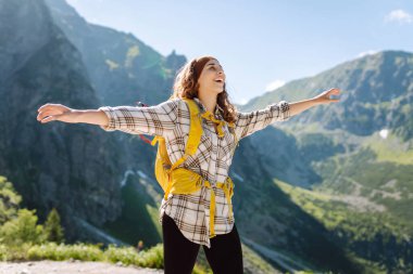 Dağ manzarasına tepeden bakan parlak sırt çantalı bir kadın yürüyüşçü. Genç bir kadın dışarıda özgürlüğün tadını çıkarıyor. Yürüyüş kavramı.