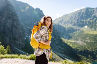 Dağ manzarasına tepeden bakan parlak sırt çantalı bir kadın yürüyüşçü. Genç bir kadın dışarıda özgürlüğün tadını çıkarıyor. Yürüyüş kavramı.