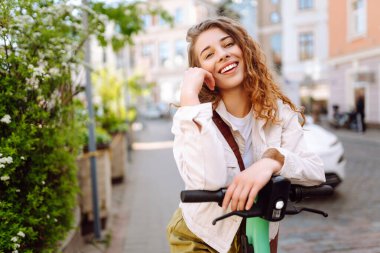 Elektrikli scooter kullanan güzel bir turist güneşli caddelerde geziyor. Genç bir kadın seyahat etmeyi, hafta sonlarını ve dışarıda yürümeyi seviyor. Yaşam biçimi.