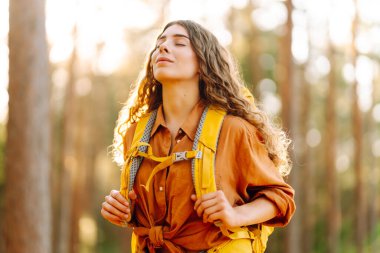 Sarı sırt çantalı, özgürlüğünü hisseden ve yürüyüş yaparken güneşli havanın tadını çıkaran genç bir kadının portresi. Seyahat, boş zaman, özgürlük konsepti. Etkin yaşam biçimi.