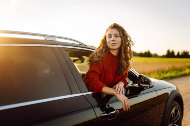 Araba camından sarkan tatlı bir kadın. Gün batımında arabadaki güzel bayan gezgin. Özgürlük kavramı. Etkin yaşam biçimi.