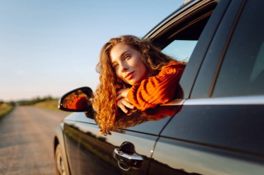 Araba camından sarkan tatlı bir kadın. Gün batımında arabadaki güzel bayan gezgin. Özgürlük kavramı. Etkin yaşam biçimi.