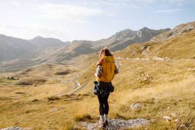 Yürüyüş kıyafetleri içindeki neşeli turistin dağ manzaralı özgürlüğünü hissetmesi. Tepede yürüyüş yapan genç bir kadın. Özgürlük, macera konsepti.