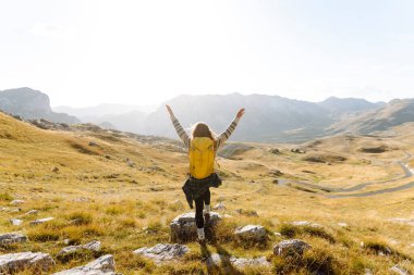 Yürüyüş kıyafetleri içindeki neşeli turistin dağ manzaralı özgürlüğünü hissetmesi. Tepede yürüyüş yapan genç bir kadın. Özgürlük, macera konsepti.