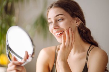 Güzel bir kadın parmaklarıyla tenine dokunur ve aynadaki yansımasından zevk alır. Sivilceli ve döküntülü genç bir kadının cildine yakın çekim. Güzellik konsepti.