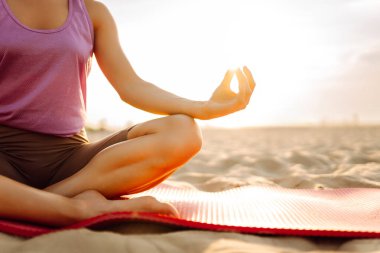 Sportif kadın gün batımı plajında yoga minderinde esneme egzersizi yapıyor. Spor kıyafetleriyle dışarıda egzersiz yapan güzel bir kadın. Spor, eğlence konsepti.