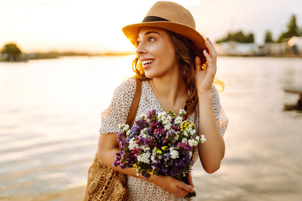 Молодая женщина смеется с букетом диких цветов на закате. Цветочный турист наслаждается морской пейзаж с букет цветов на открытом воздухе. Концепция наслаждения и расслабления.