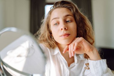 Genç bir kadının yüzünün cildindeki kızarıklıklara dokunuşunu yakından çek. Güzel bir kadın aynada yansımasından hoşlanır. Güzellik ve doğallık kavramı.