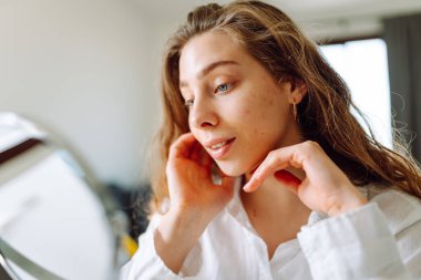 Genç bir kadının yüzünün cildindeki kızarıklıklara dokunuşunu yakından çek. Güzel bir kadın aynada yansımasından hoşlanır. Güzellik ve doğallık kavramı.