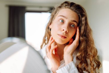 Genç bir kadının yüzünün cildindeki kızarıklıklara dokunuşunu yakından çek. Güzel bir kadın aynada yansımasından hoşlanır. Güzellik ve doğallık kavramı.