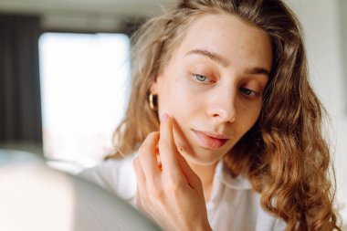 Genç bir kadının yüzünün cildindeki kızarıklıklara dokunuşunu yakından çek. Güzel bir kadın aynada yansımasından hoşlanır. Güzellik ve doğallık kavramı.