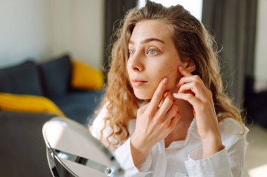 Genç bir kadının yüzünün cildindeki kızarıklıklara dokunuşunu yakından çek. Güzel bir kadın aynada yansımasından hoşlanır. Güzellik ve doğallık kavramı.