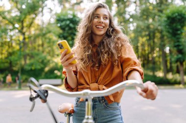 Parktaki güneşli sokakta bisiklet süren gülümseyen bir kadın. Genç bir kadın güneşli günün tadını çıkarıyor ve dışarıda eğleniyor. Hafta sonu ve günlük tutma kavramı.