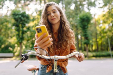 Parktaki güneşli sokakta bisiklet süren gülümseyen bir kadın. Genç bir kadın güneşli günün tadını çıkarıyor ve dışarıda eğleniyor. Hafta sonu ve günlük tutma kavramı.