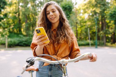 Parktaki güneşli sokakta bisiklet süren gülümseyen bir kadın. Genç bir kadın güneşli günün tadını çıkarıyor ve dışarıda eğleniyor. Hafta sonu ve günlük tutma kavramı.