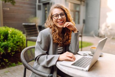 Dürbünlü güzel bir kadın dışarıda, masada çalışıyor. Kafede dizüstü bilgisayarı olan serbest çalışan bir kadın havanın tadını çıkarıyor. Teknoloji konsepti, uzaktan çalışma.