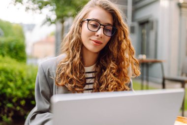 Dürbünlü güzel bir kadın dışarıda, masada çalışıyor. Kafede dizüstü bilgisayarı olan serbest çalışan bir kadın havanın tadını çıkarıyor. Teknoloji konsepti, uzaktan çalışma.