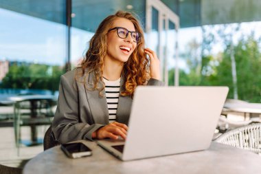 Dürbünlü güzel bir kadın dışarıda, masada çalışıyor. Kafede dizüstü bilgisayarı olan serbest çalışan bir kadın havanın tadını çıkarıyor. Teknoloji konsepti, uzaktan çalışma.