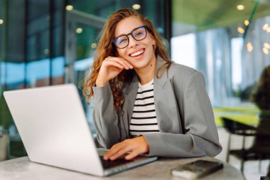 Dürbünlü güzel bir kadın dışarıda, masada çalışıyor. Kafede dizüstü bilgisayarı olan serbest çalışan bir kadın havanın tadını çıkarıyor. Teknoloji konsepti, uzaktan çalışma.