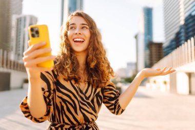 Metropolis manzaralı telefon yürüyüşleri yapan güzel bir turist. Gün batımında telefonlu genç kadın blogları. Seyahat, tatil ve blog konsepti.