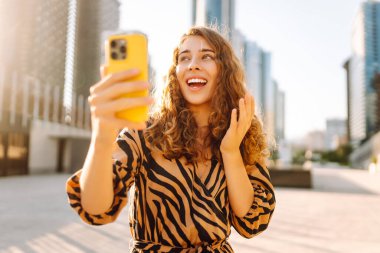 Metropolis manzaralı telefon yürüyüşleri yapan güzel bir turist. Gün batımında telefonlu genç kadın blogları. Seyahat, tatil ve blog konsepti.