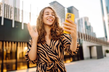 Metropolis manzaralı telefon yürüyüşleri yapan güzel bir turist. Gün batımında telefonlu genç kadın blogları. Seyahat, tatil ve blog konsepti.