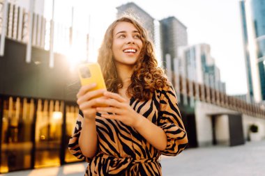 Metropolis manzaralı telefon yürüyüşleri yapan güzel bir turist. Gün batımında telefonlu genç kadın blogları. Seyahat, tatil ve blog konsepti.