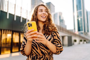 Metropolis manzaralı telefon yürüyüşleri yapan güzel bir turist. Gün batımında telefonlu genç kadın blogları. Seyahat, tatil ve blog konsepti.