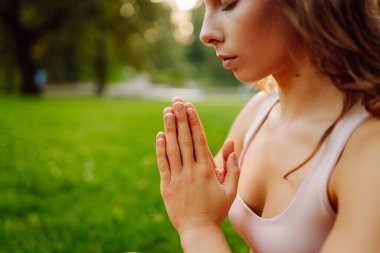 Güzel bir kadın parkta pembe bir paspasın üzerinde esneme egzersizleri yapıyor. Gün batımında meditasyon yapan genç bir kadın. Dinlenme ve rahatlama kavramı.