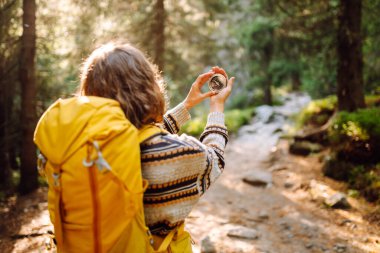 Sırt çantası ve pusula ile gün batımında yürüyüş yapan orman yolunda bir kadın yürüyüşçünün arka görüntüsü. Genç bayan pusula ile yol tarifi arıyor. Etkin yaşam biçimi.