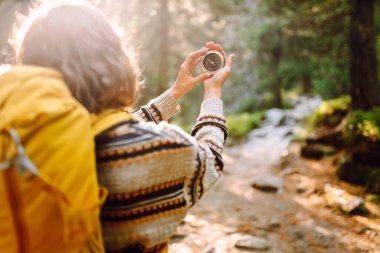 Sırt çantası ve pusula ile gün batımında yürüyüş yapan orman yolunda bir kadın yürüyüşçünün arka görüntüsü. Genç bayan pusula ile yol tarifi arıyor. Etkin yaşam biçimi.