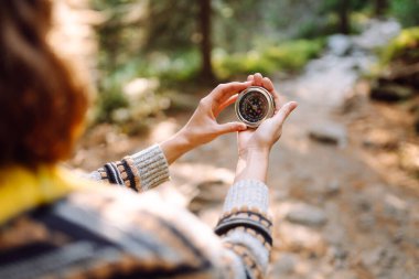 Sırt çantası ve pusula ile gün batımında yürüyüş yapan orman yolunda bir kadın yürüyüşçünün arka görüntüsü. Genç bayan pusula ile yol tarifi arıyor. Etkin yaşam biçimi.