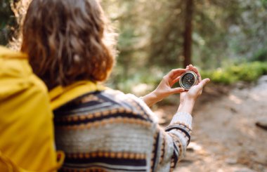 Sırt çantası ve pusula ile gün batımında yürüyüş yapan orman yolunda bir kadın yürüyüşçünün arka görüntüsü. Genç bayan pusula ile yol tarifi arıyor. Etkin yaşam biçimi.