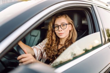 Güzel bir kadın araba kullanıyor, gezintiden zevk alıyor. Gün batımında gözlüklü genç bayan sürücü. Ulaşım ve eğlence kavramı.