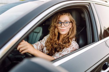 Güzel bir kadın araba kullanıyor, gezintiden zevk alıyor. Gün batımında gözlüklü genç bayan sürücü. Ulaşım ve eğlence kavramı.